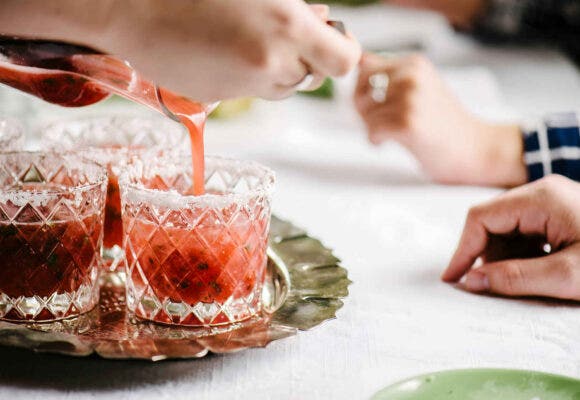 Close up on a person pouring a batch of strawberry margaritas into glasses