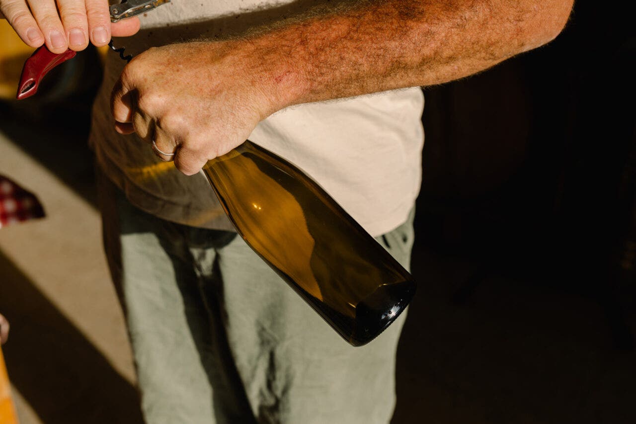 A close-up of an unidentified man using a corkscrew to open a bottle of organic wine inside a small, family-owned winery.