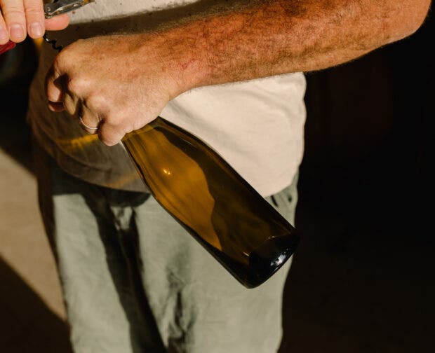 A close-up of an unidentified man using a corkscrew to open a bottle of organic wine inside a small, family-owned winery.