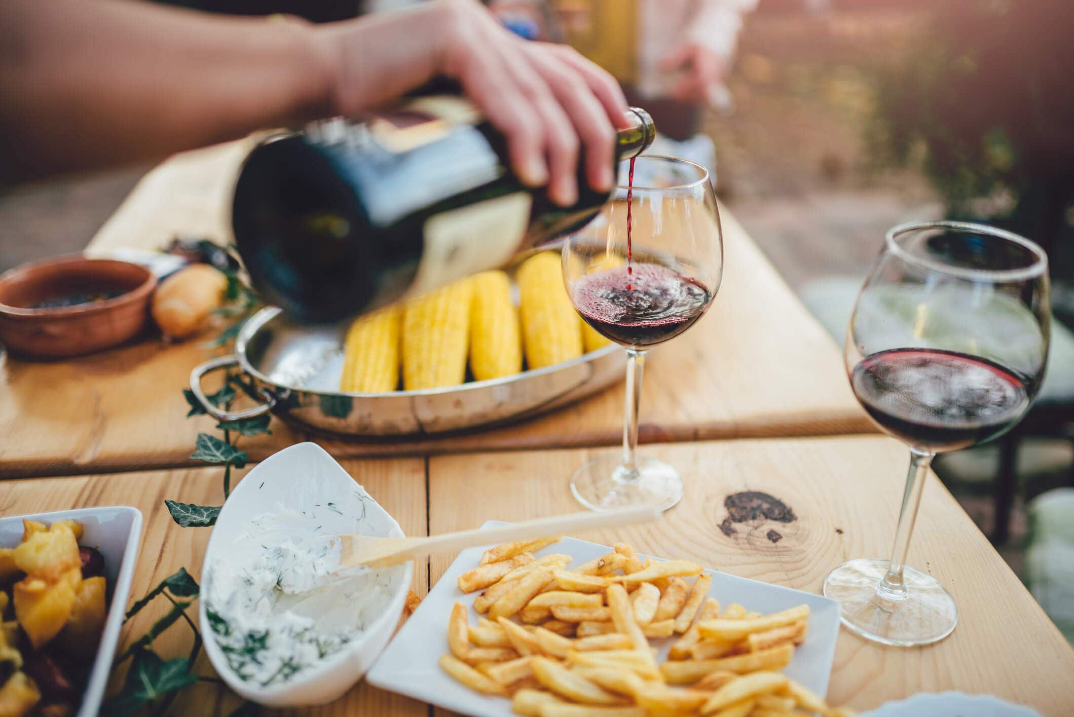 Man pouring red wine at a backyard table