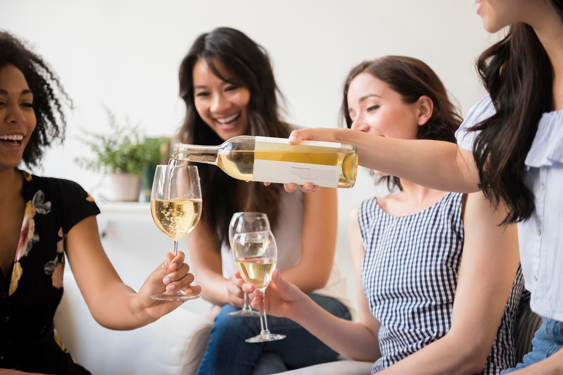 An image of woman pouring bottle of white wine for friends_GettyImages-685010941_