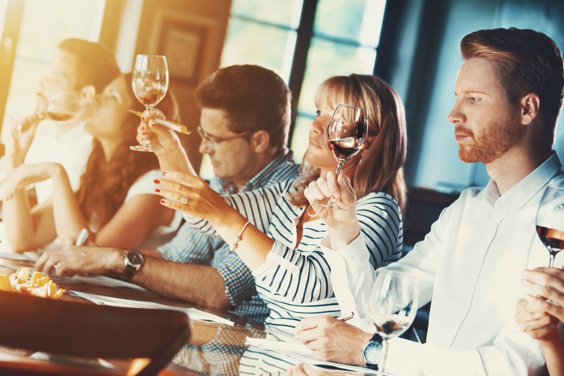 Three people examining wine in glasses and writing things